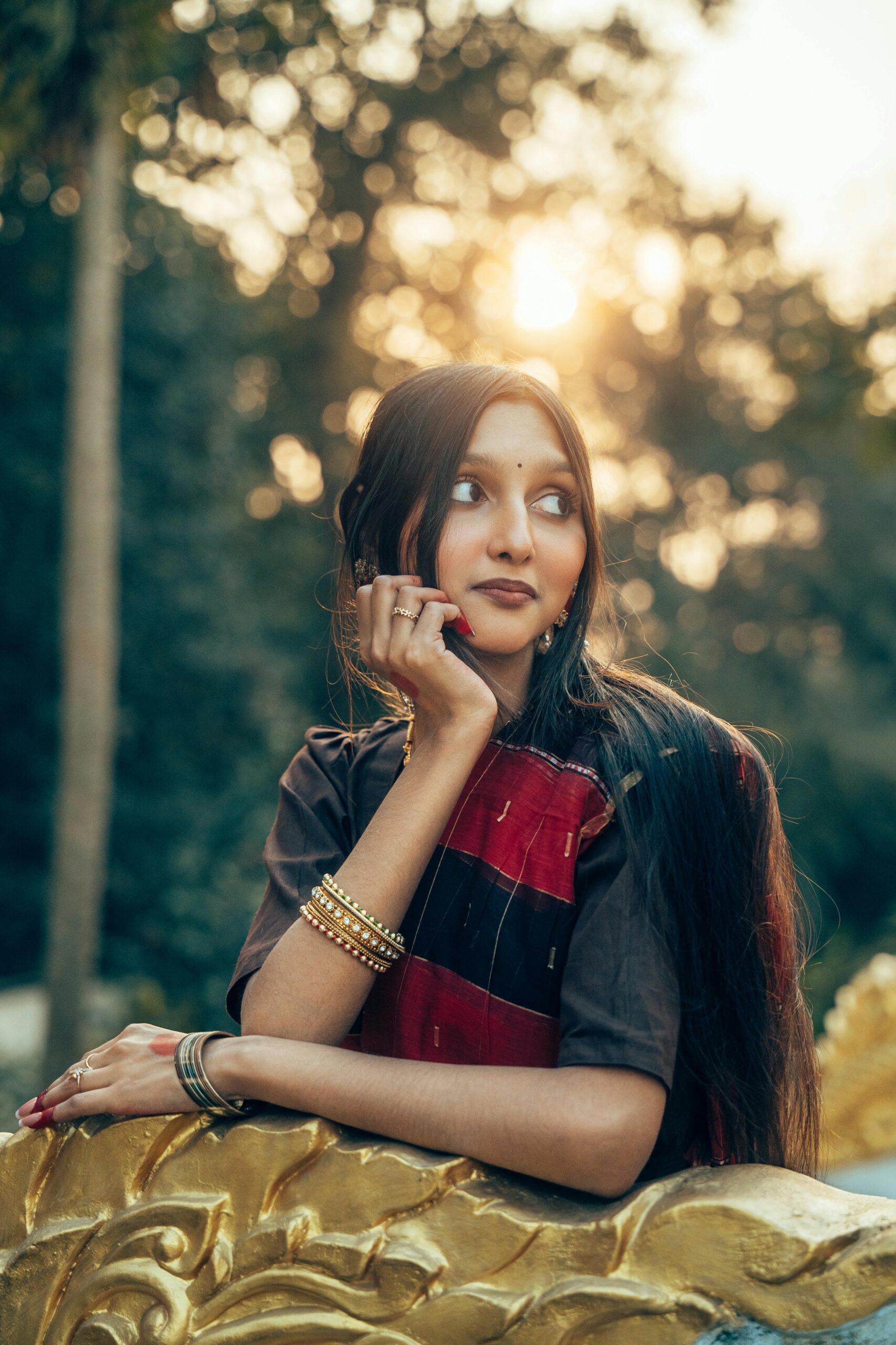 A young woman in a red saree poses elegantly outdoors at sunset in Cumilla, Bangladesh.