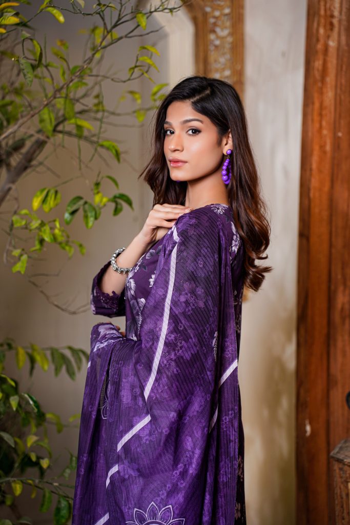 A fashionable woman in Lahore wearing a purple dress posing indoors with natural elements.